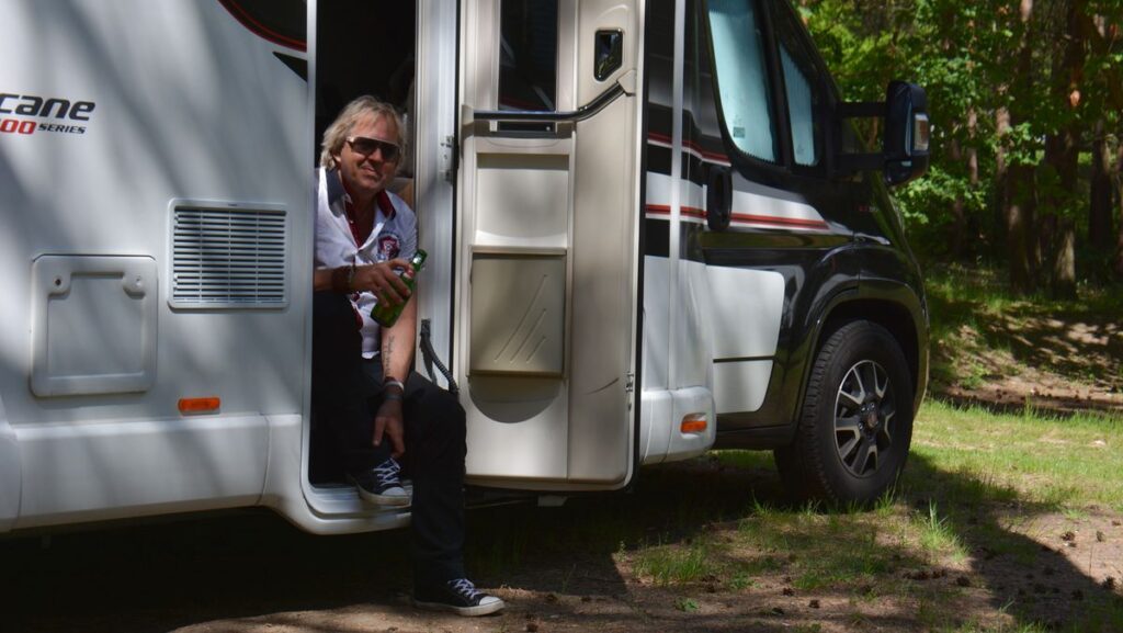A man sits with a beer in hand in the doorway to the living area of a motorhome