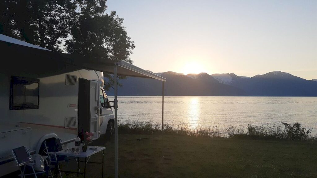 A motorhome with the awning extended, parked by the water